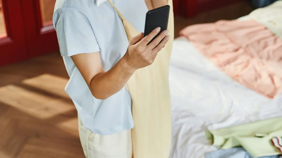 Woman holding a dress and using her phone to prepare a Vinted description